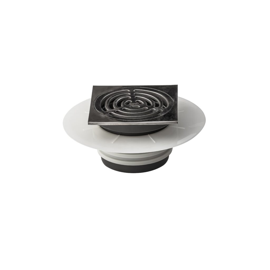 A metal floor drain with a circular grate and a square frame, attached to a white and black plastic base, isolated on a white background.